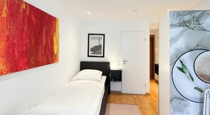 Quarto com uma cama, mesa de cabeceira, quadro emoldurado e porta que dá para outro espaço.