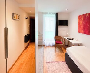 Quarto de hotel com cama, escrivaninha, cadeira, televisão e janela com cortinas.