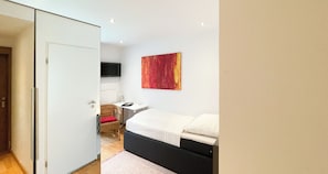 A bedroom with a bed, a television on the wall, and a door leading to another room.