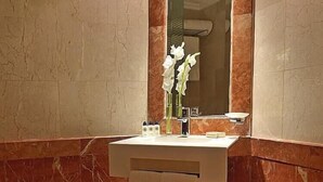 Une salle de bain avec un mur en marbre, un lavabo avec un miroir, des toilettes et une poubelle.