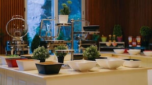 Un buffet composé de différents plats et de saladiers, d’un présentoir à étages et de plantes en pot.