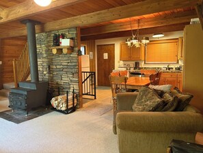A cozy living room with a stone fireplace, a dining area with wooden furniture, and a kitchen with wooden cabinets and a built-in oven. - Cozy & Secluded Forest Staycation-BBQ (Brighton)