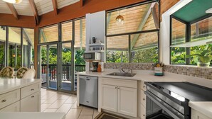 Una cocina moderna con lavavajillas, microondas y estufa, ventanas amplias y vistas a zonas verdes.