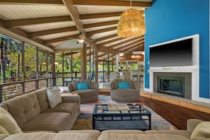 A spacious living area with a fireplace, comfortable seating, and large windows overlooking a lush garden. - Mauna Kai 7B by Gather | Princeville 3BR + Loft Condo w/ Shared Pool (Princeville)