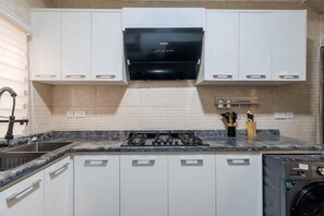 Een kleine keuken met witte kasten, een zwarte kookplaat en een inbouwmagnetron boven het aanrecht.