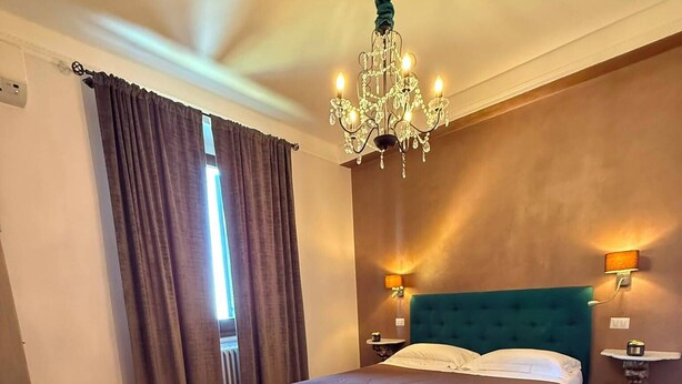 A bedroom with a bed, a chandelier, a nightstand, a wall-mounted shelf, and a potted plant. - La Rocca Guest House & SPA - Standard Room 1 (Montefalco)