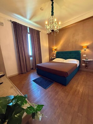 A bedroom with a bed, a chandelier, a nightstand, a wall-mounted shelf, and a potted plant. - La Rocca Guest House & SPA - Standard Room 1 (Montefalco)