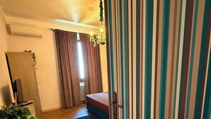 A room with a bed, a radiator, a plant, and a striped curtain. - La Rocca Guest House & SPA - Standard Room 1 (Montefalco)