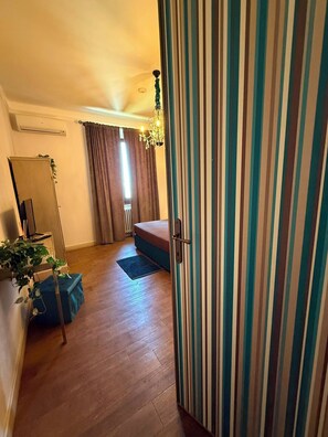 Een kamer met een bed, een radiator, een plant en een gestreept gordijn.