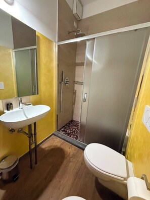 Een badkamer met een wit wastafelmeubel, toilet en douchecabine met glazen deur.