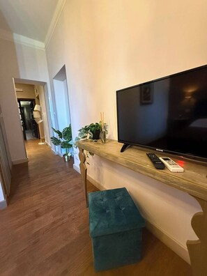 A hallway with a wooden floor, a television on a shelf, a remote control, and a bench. - La Rocca Guest House & SPA - Standard Room 1 (Montefalco)