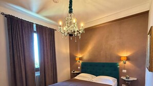A bedroom with a large bed, a chandelier, two bedside lamps, and a view of the outdoors. - La Rocca Guest House & SPA - Standard Room 1 (Montefalco)