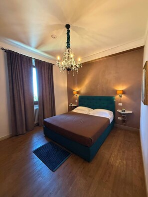 Een slaapkamer met een groot bed, een kroonluchter, twee bedlampen en uitzicht op het omliggende landschap.