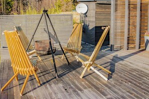 Eine Holzterrasse mit drei Holzstühlen und einer Metall-Schaukel.