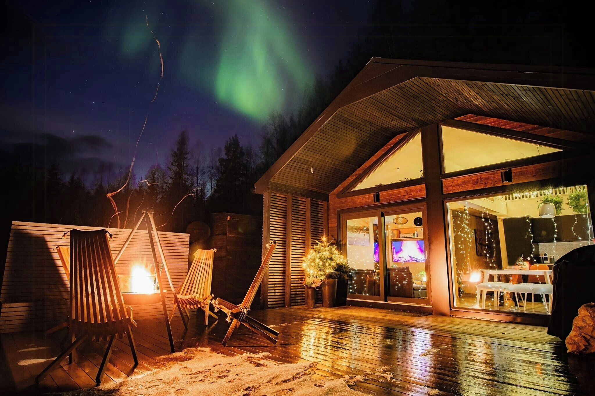 A wooden cabin with a glass door entrance, a fire pit, and a chair outside.