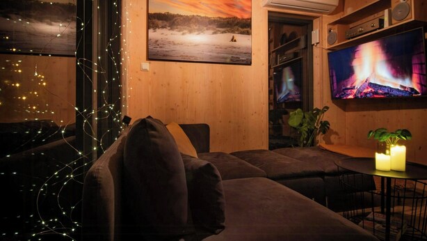 A cozy living room with a large flat-screen TV, a fireplace, and a window with string lights. - Modern cabin by Krøderfjorden near Norefjell (Noresund)