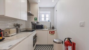 Eine kompakte Küche mit weißen Schränken, einer Mikrowelle, einem Toaster und einem Feuerlöscher.