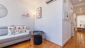 Ein modernes Wohnzimmer mit einem grauen Sofa, dekorativen Kissen, einem runden Tisch und einem schwarzen Hocker.