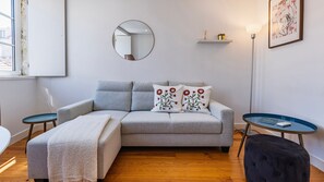 Ein modernes Wohnzimmer mit einem grauen Sofa, zwei Beistelltischen, einem runden Spiegel und einem gerahmten Kunstwerk an der Wand.
