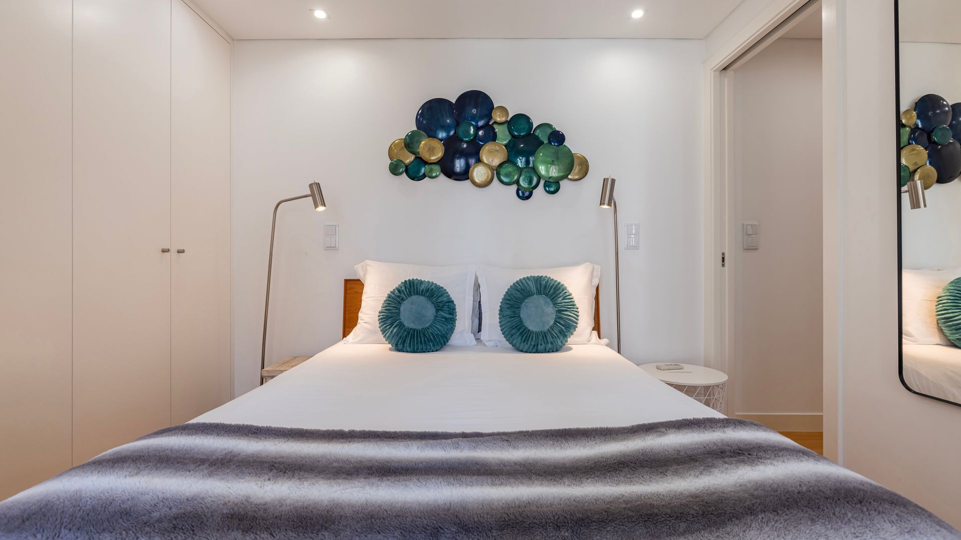 Une chambre à coucher comprenant un lit, deux lampes de chevet, un luminaire fixé au mur et un miroir.