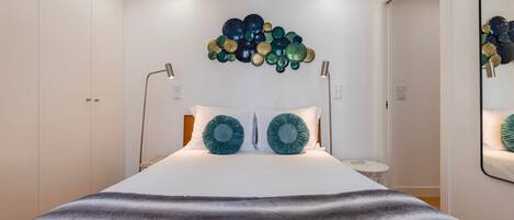 Une chambre à coucher comprenant un lit, deux lampes de chevet, un luminaire fixé au mur et un miroir.