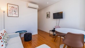 Ein modernes Wohnzimmer mit einer Couch, einem runden Tisch, einem Flachbildfernseher und einer Klimaanlage.