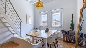 A modern dining area with a wooden table, white chairs, and a hanging light fixture. - 2BR Beachside Living by LovelyStay (Costa da Caparica)