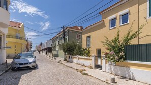 A cobblestone street lined with colorful buildings, a parked car, and overhead power lines. - 2BR Beachside Living by LovelyStay (Costa da Caparica)