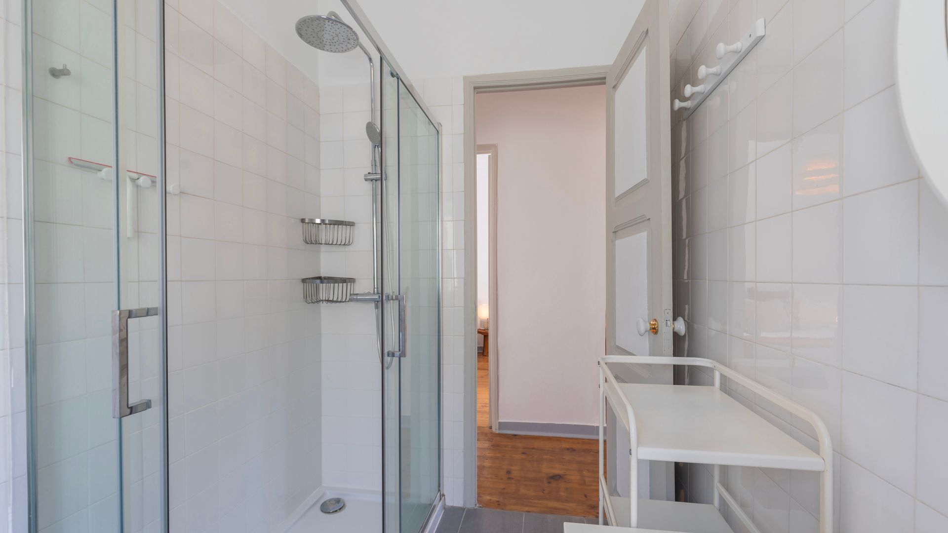 A modern bathroom with a glass shower enclosure, a white sink with a mirror, and a wooden floor.