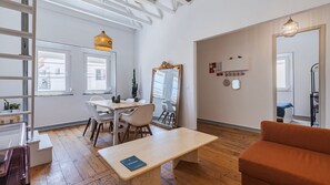 A modern living room with a wooden table, a sofa, and a dining area with chairs and a cactus plant. - 2BR Beachside Living by LovelyStay (Costa da Caparica)