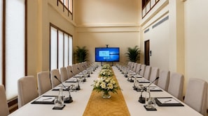 A conference room with a long table, chairs, microphones, and a screen at the front.
