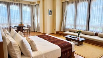 A hotel room with a large bed, a sofa, a coffee table, and a dining area with a table and chairs.