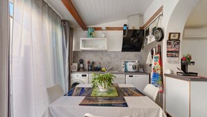A compact kitchen with a dining area, featuring a washing machine, microwave, and a small refrigerator. - Villa Rosina with Private Terrace, Wi-Fi, and Air Conditioning (Gruissan)