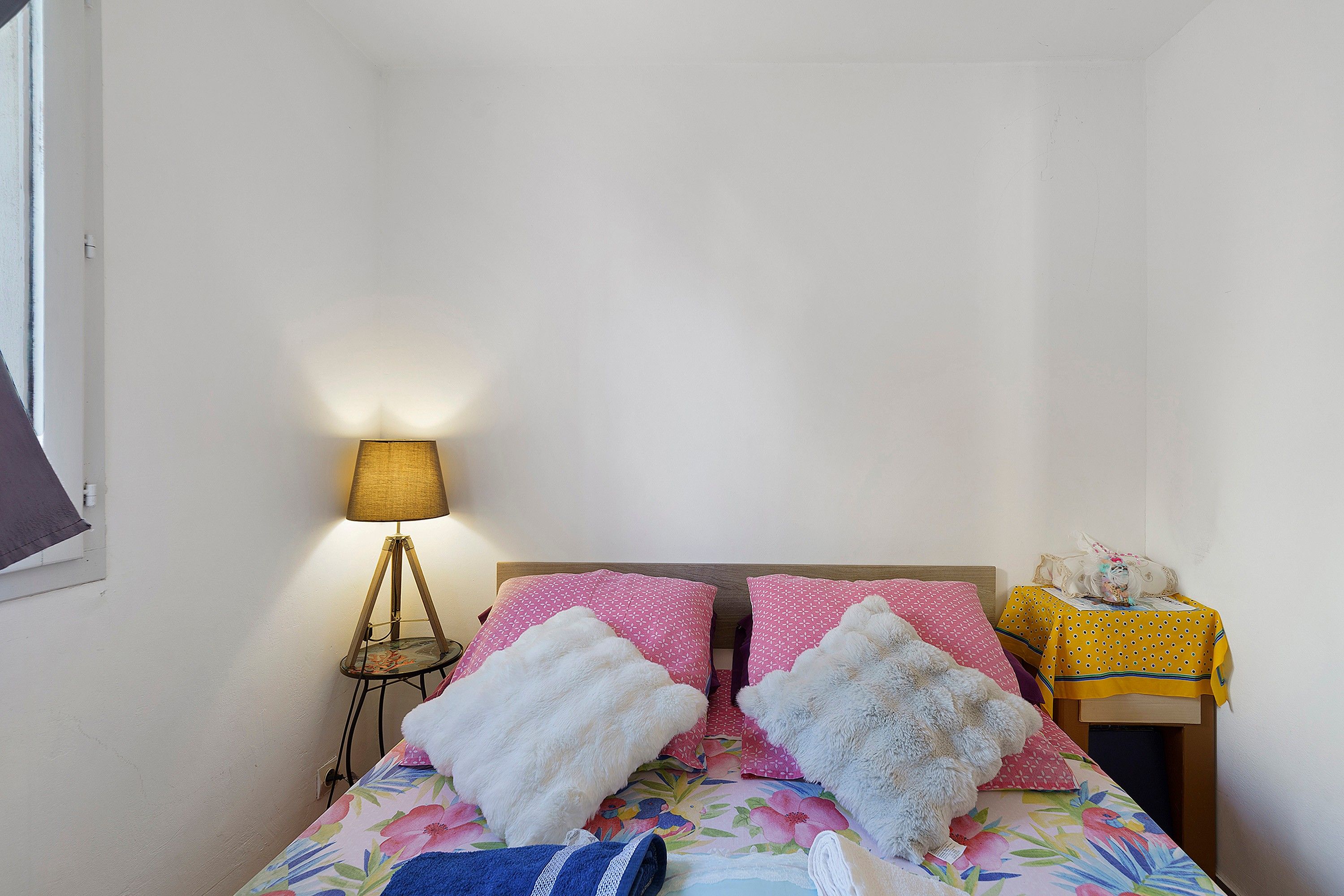 Et værelse med en seng, et natbord, en lampe og et lille bord med et gult dug.