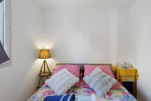A room with a bed, a bedside table, a lamp, and a small table with a yellow tablecloth.
