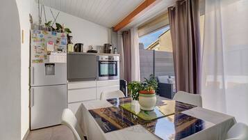 A compact kitchen with a refrigerator, oven, and a dining table with chairs.
