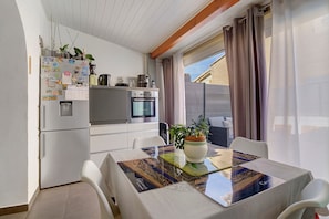 Cocina compacta con refrigerador, horno y una mesa de comedor con sillas.