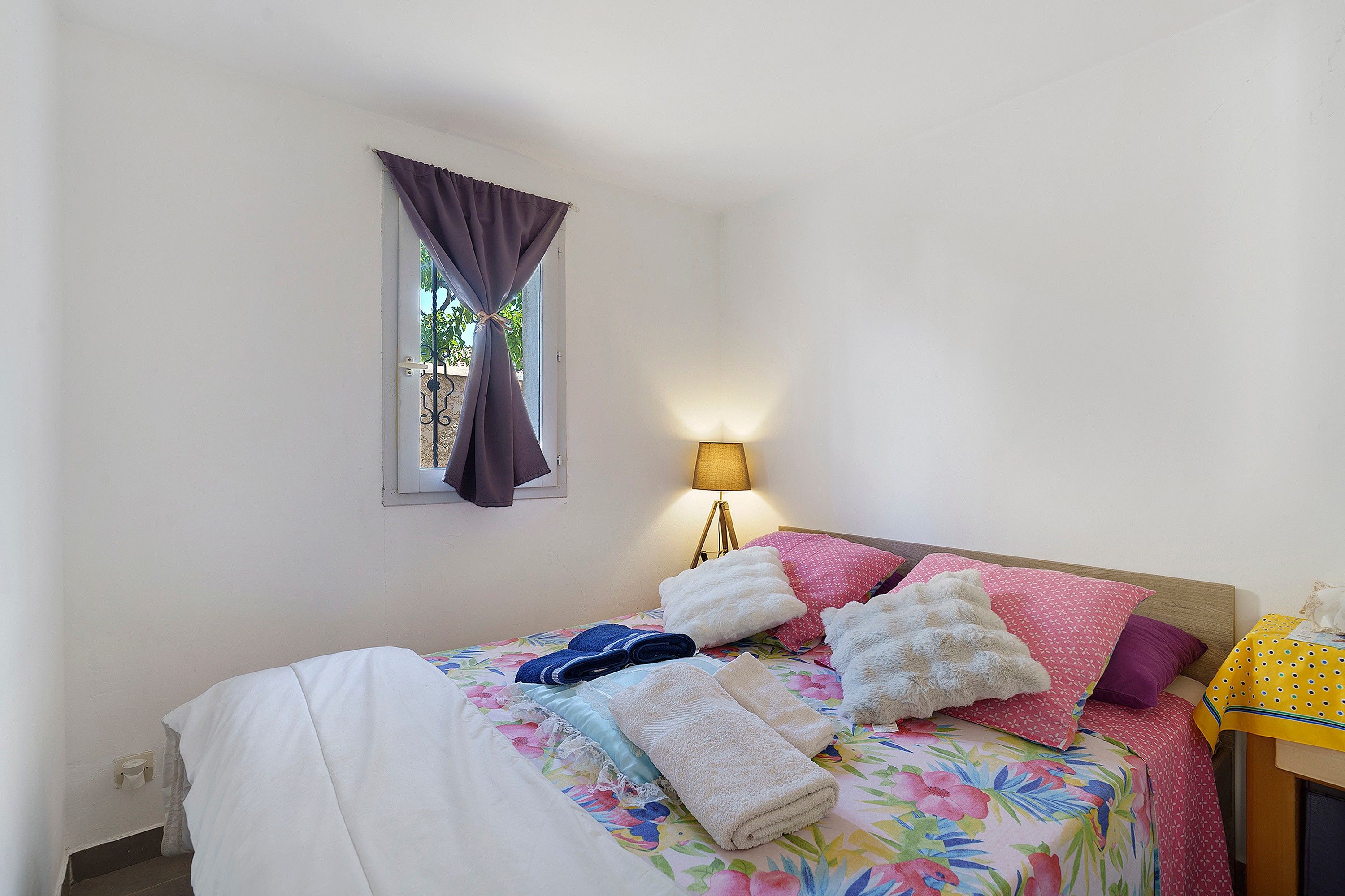 A bedroom with a bed, pillows, a lamp, and a window with curtains.