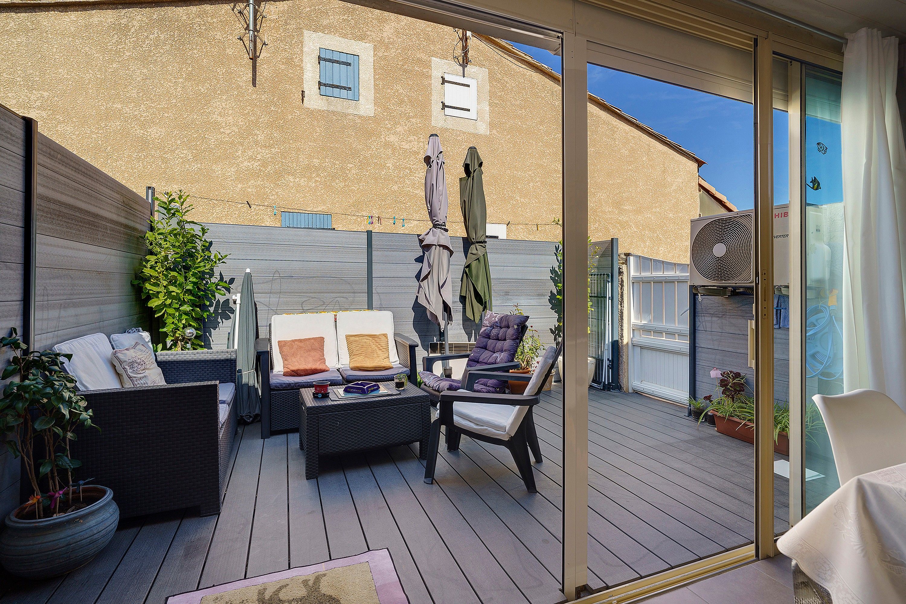 Een overdekt terras met rieten meubels, een tafel en potplanten.