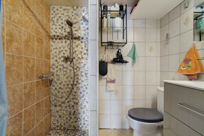 A bathroom with a shower, toilet, and a towel rack with various items.