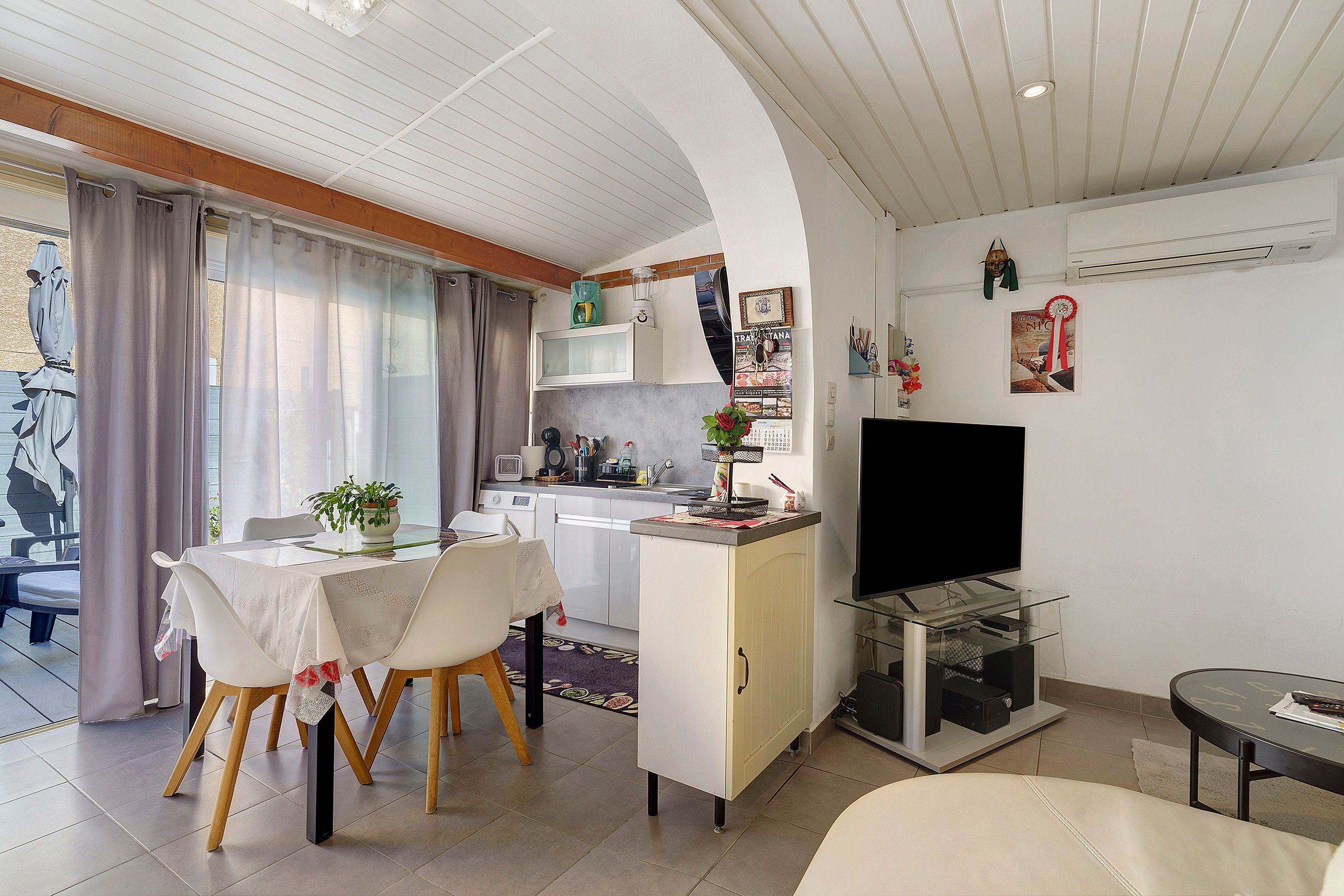 A compact living space with a dining area, kitchenette, and a flat-screen TV.