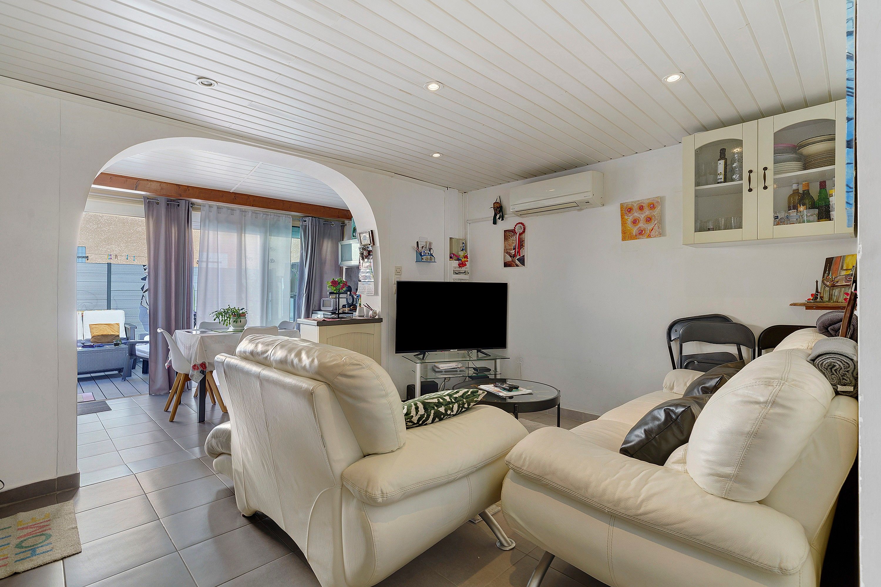 En stue med sofa, fjernsyn og spiseplads med bord og stole.