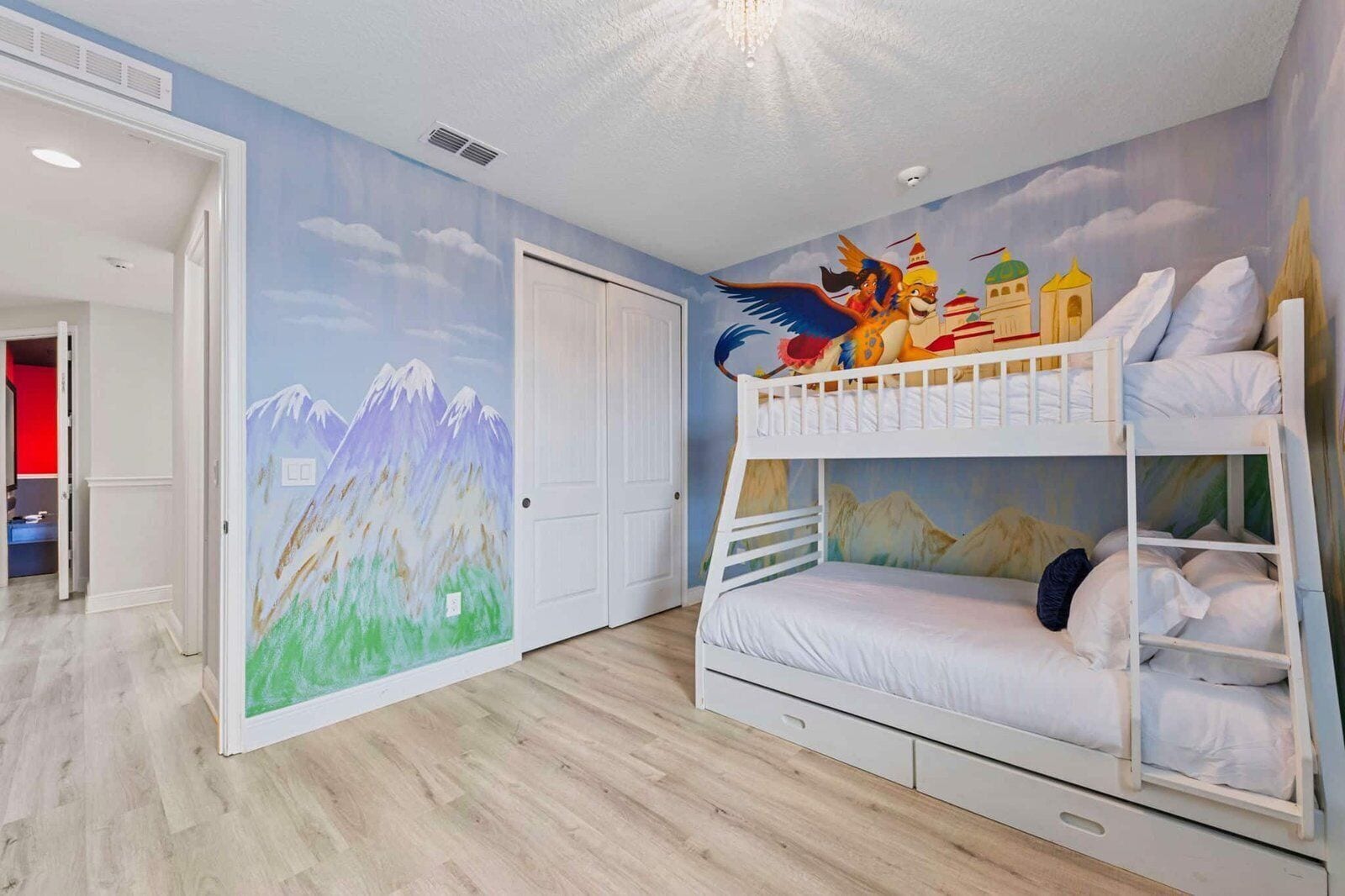 Une chambre d’enfant avec des lits superposés, une porte et une fresque murale.