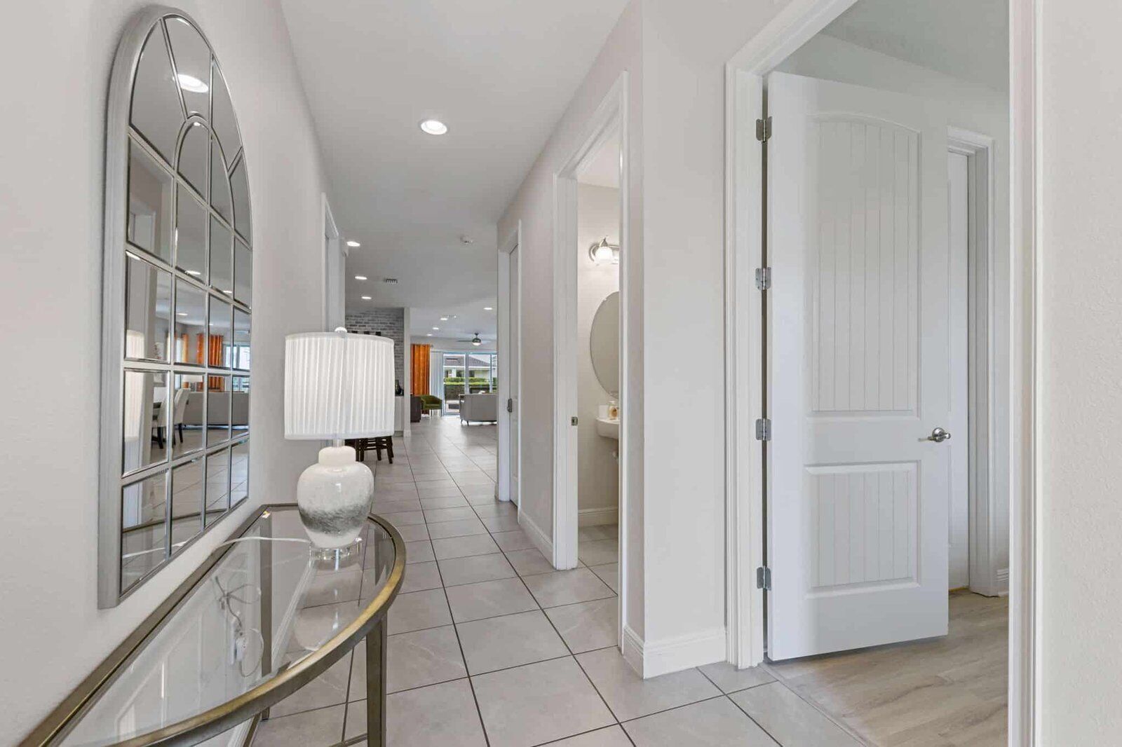 A modern hallway with a glass-top table, a lamp, and a door leading to a bathroom.