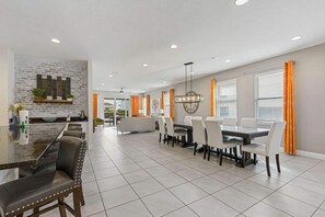 A spacious dining area with a long table and multiple chairs, a kitchen area with a brick backsplash, and a ceiling fan. - Harmony Palms Villa - Eight Bedroom House, Sleeps 17 (Lake Buena Vista)