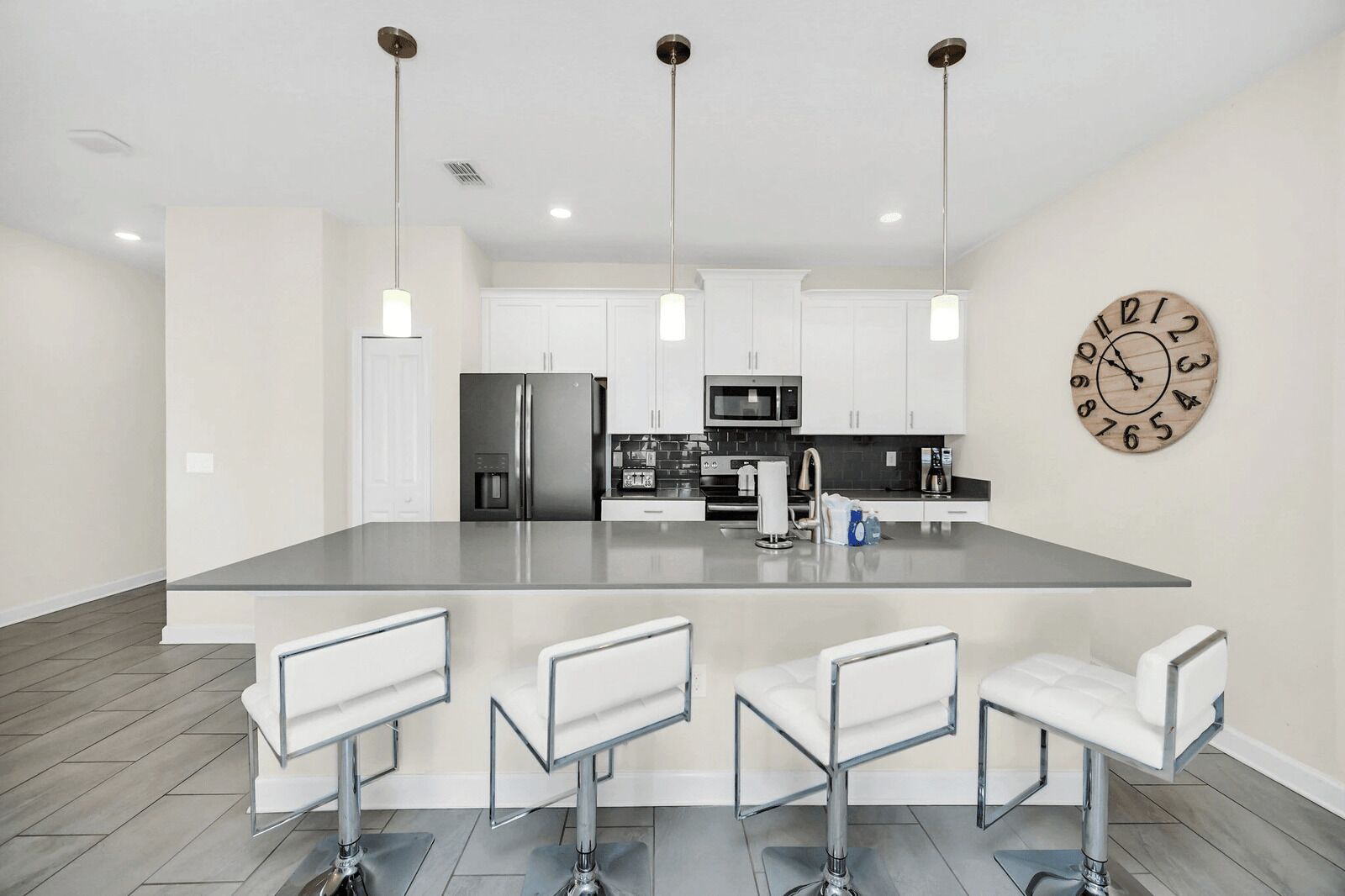 Una cocina moderna con una isla central, taburetes de bar, electrodomésticos de acero inoxidable y un reloj de pared.