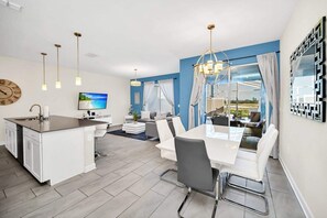 A modern kitchen with a central island, a dining area with a white table and chairs, and a living area with a sofa and a TV. - Amazing resort facilites, lazy river- resort pools-9 miles Disney-free wifi (Kissimmee)