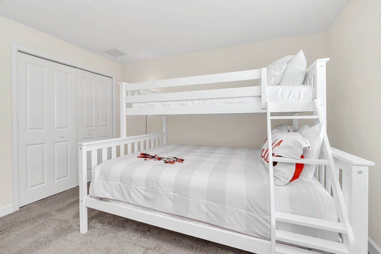 A bunk bed with a white frame and grey bedding, a white door, and a carpeted floor.