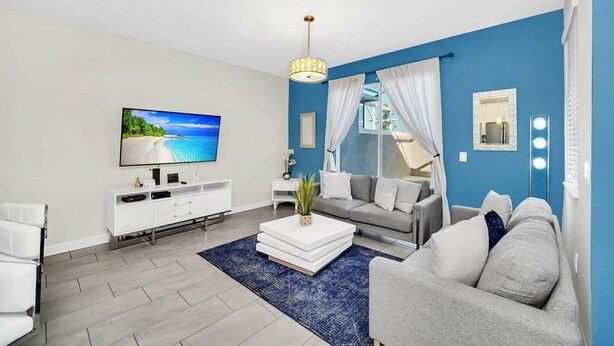 A modern living room with a flat-screen TV, a white entertainment unit, a grey sofa, a white coffee table, and a blue accent wall. - Sunshine Escape - Four Bedroom House, Sleeps 8 (Kissimmee)
