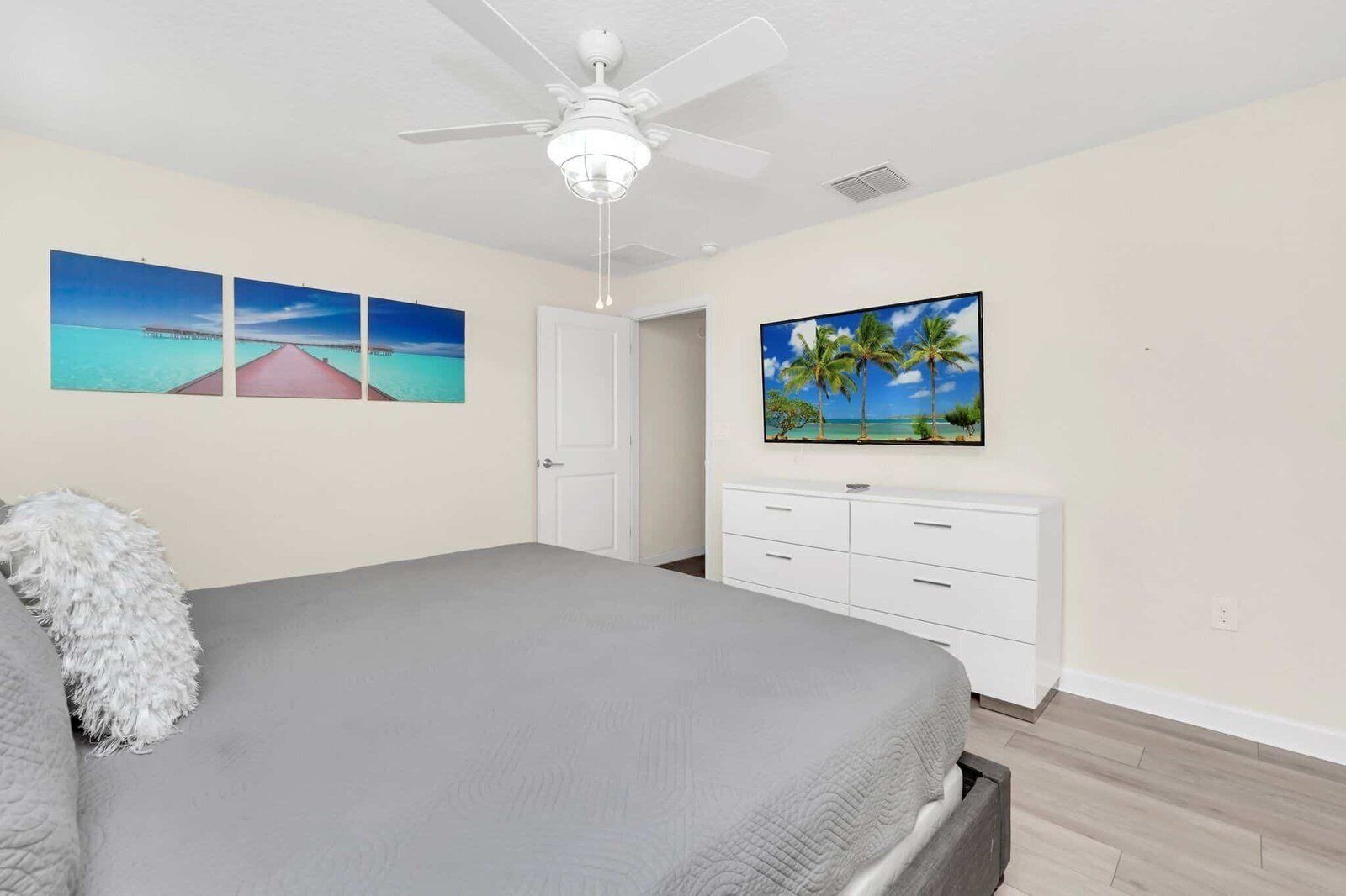 A bedroom with a bed, a ceiling fan, a white dresser, and two wall-mounted paintings.